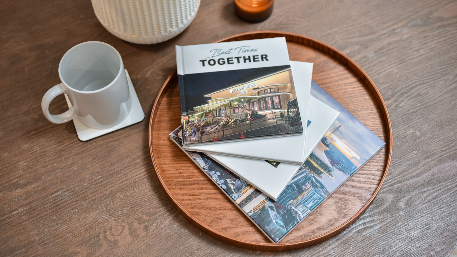 Image ofthree photobooks stacked on top of each other on a round wooden tray thats placed on a coffee table.